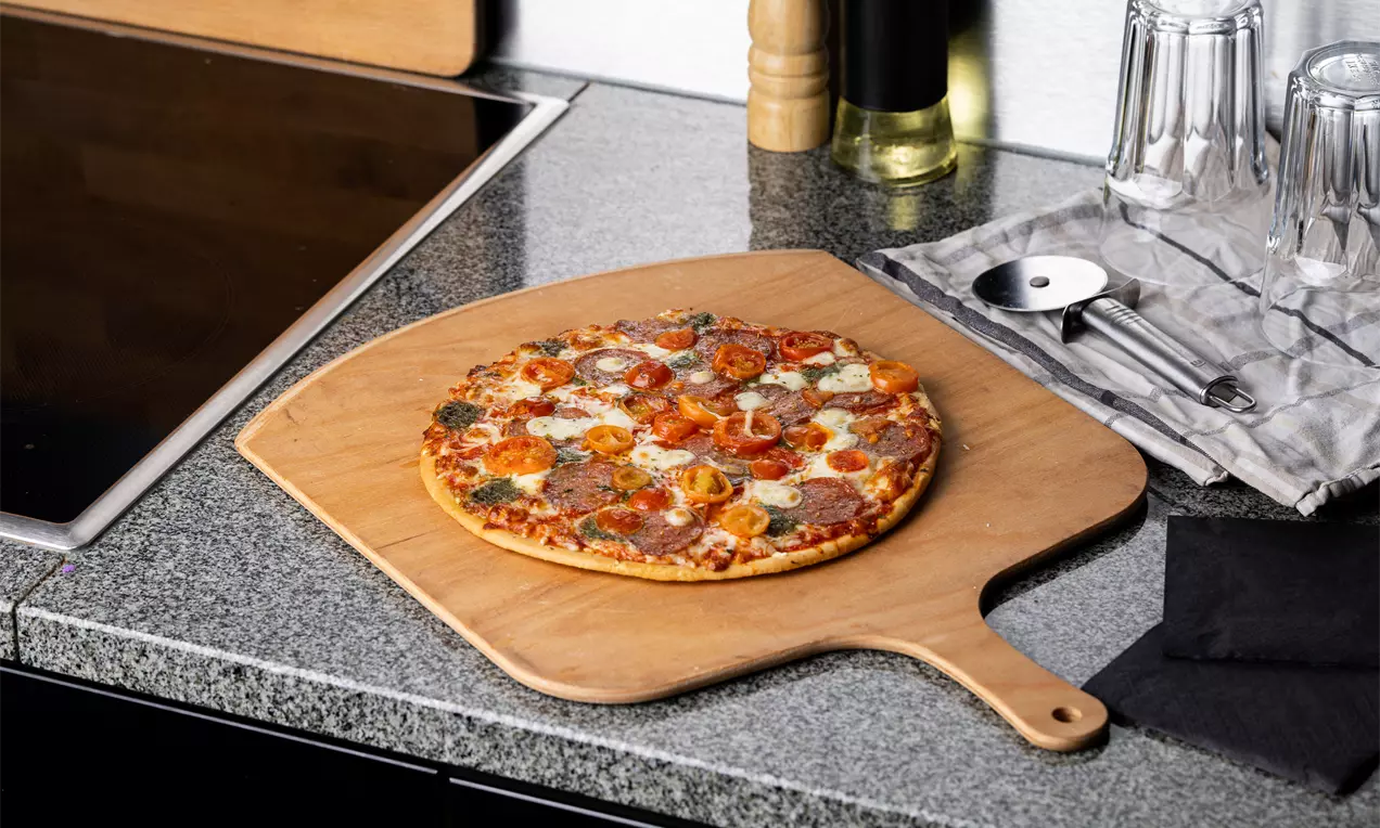 Ohut, pyöreä pizza ruskistuneella pohjalla, sulanut juusto ja värikkäät täytteet aseteltuna vaalealle puulapiolle harmaalla tasolla
