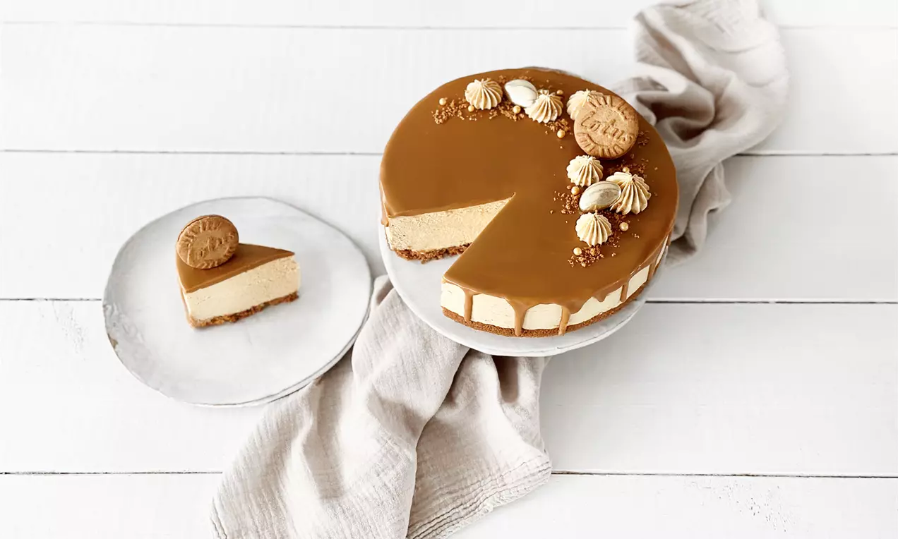 Vaniljainen Biscoff-kakku kerrostuu ruskeaan keksipohjaan ja vaaleaan täytteeseen, sileä karamellipinta koristeltu keksillä ja kreemillä valkoisella lautasella