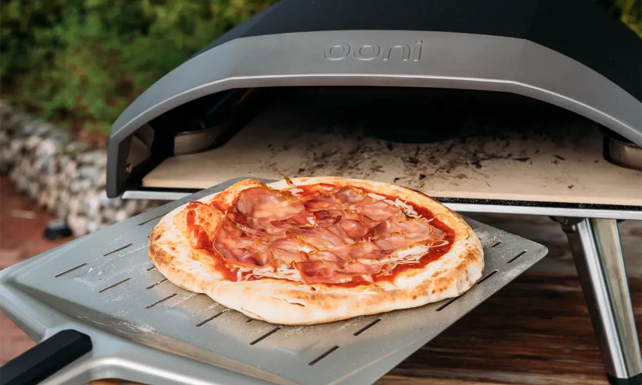 Vaaleanpunaisilla kinkkusiivuilla ja kirkkaanpunaisella tomaattikastikkeella täytetty pizza kultaisen kuoren ympäröimänä metallilastalla