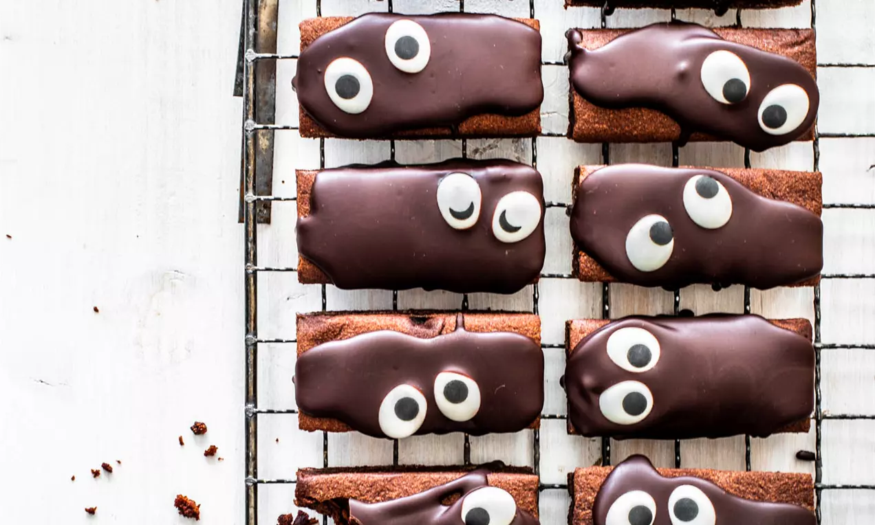 Pitkät, tummasuklaiset brownie-palat silmäkoristeilla, aseteltuina rivissä metalliritilälle valkoisella taustalla